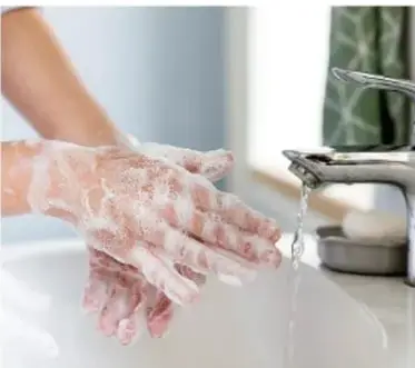 Manos lavándose con abundante espuma bajo el chorro de una llave, mostrando el lavado de manos previo a la higiene digestiva.