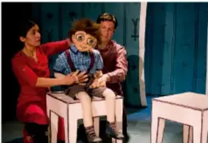 Fotografía de una obra teatral con actores y un títere en escena, etiquetada 'Teatro'.