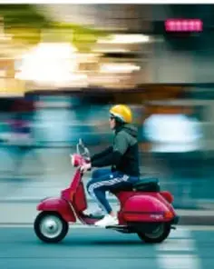 Fotografía de una persona conduciendo una motocicleta roja en la ciudad, con efecto de movimiento.