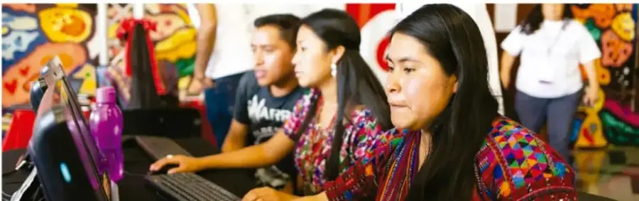 Fotografía de mujeres indígenas en traje tradicional trabajando con computadoras, ilustrando el uso de tecnologías para el desarrollo de lenguas indígenas.