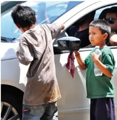 Fotografía de dos niños trabajando en la calle limpiando o vendiendo a los ocupantes de un automóvil, ilustrando el trabajo infantil.