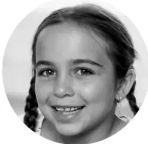 Fotografía en blanco y negro de una niña sonriente con trenzas, mirando a la cámara.