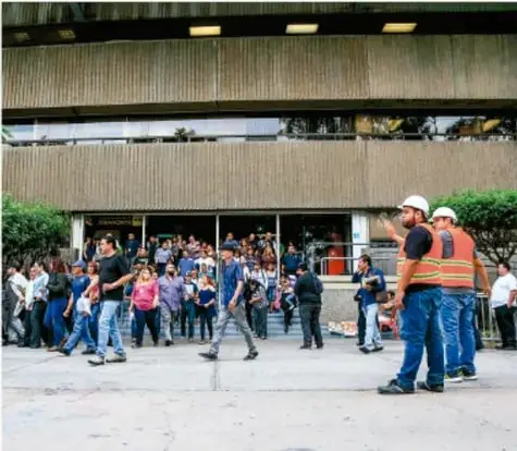 Fotografía de personal de Protección Civil con chalecos naranjas dirigiendo la evacuación de un edificio.