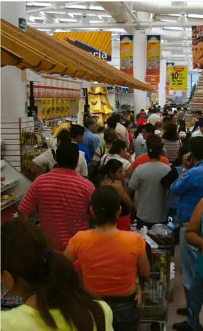 Fotografía de un supermercado lleno de consumidores empujando carritos en las filas de caja, ilustrando la sociedad de consumo.