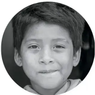 Fotografía circular en blanco y negro de un niño sonriente de primaria, probablemente el estudiante que realiza la actividad.