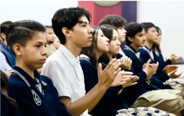 Fotografía de estudiantes de secundaria con uniforme escolar, sentados y aplaudiendo en una asamblea o acto escolar, mostrando participación comunitaria.