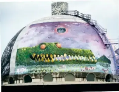 Mural pintado sobre una cúpula o techo abombado con la figura de un cocodrilo verde de grandes dientes sobre fondo morado.
