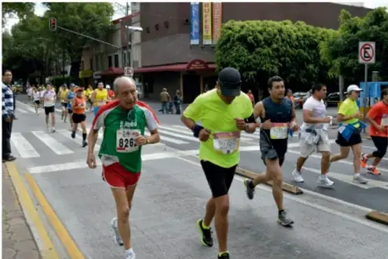 Corredores de distintas edades participando en una carrera urbana (maratón) en una calle señalizada.
