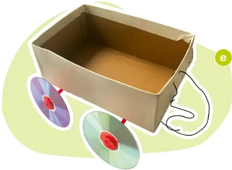 Caja de cartón con dos palos de madera que atraviesan su base; en cada extremo hay un CD sujeto con plastilina roja, formando las ruedas del carrito.