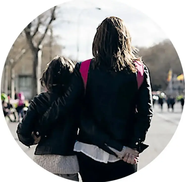 Fotografía circular de una mujer y una niña de espaldas caminando por la calle, tomadas de la mano.