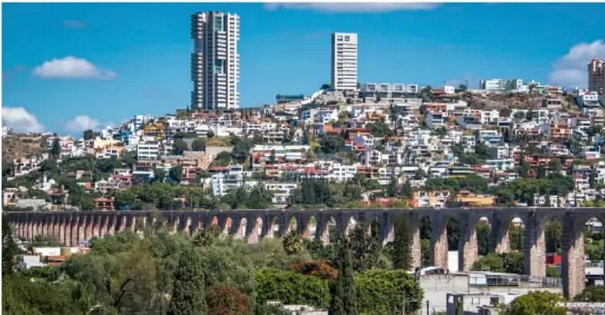 Fotografía de una ciudad densamente poblada con edificios altos, casas en laderas y un viaducto con arcos, que contrasta con el paisaje rural.