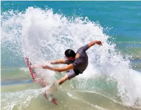 Fotografía de una surfista mujer con traje de neopreno montando una ola sobre una tabla blanca.