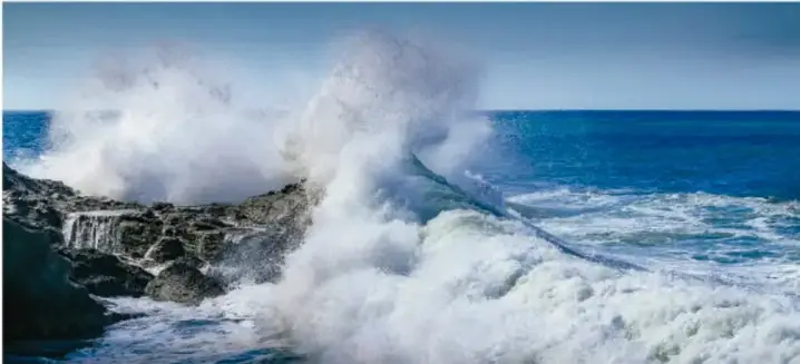 Fotografía de olas rompiendo en un acantilado, que ilustra el movimiento de las mareas.