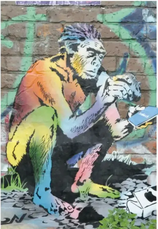 Grafiti sobre muro de ladrillo: figura de un ser prehistórico agachado, pintado en colores (naranja, verde, rosa, azul), que sostiene una lata de aerosol y pinta.