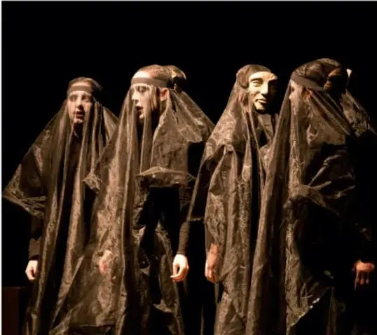 Fotografía de cuatro actores con máscaras y vestimenta oscura, representando una obra de teatro griego.