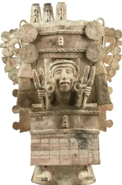 Escultura mexica de piedra con figura humana en el centro flanqueada por elementos vegetales (mazorcas) y tocado ceremonial, probablemente representación de una diosa del maíz.