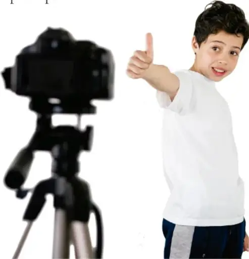 Cámara fotográfica sobre un tripié y un niño con playera blanca haciendo la señal de aprobación con el pulgar.