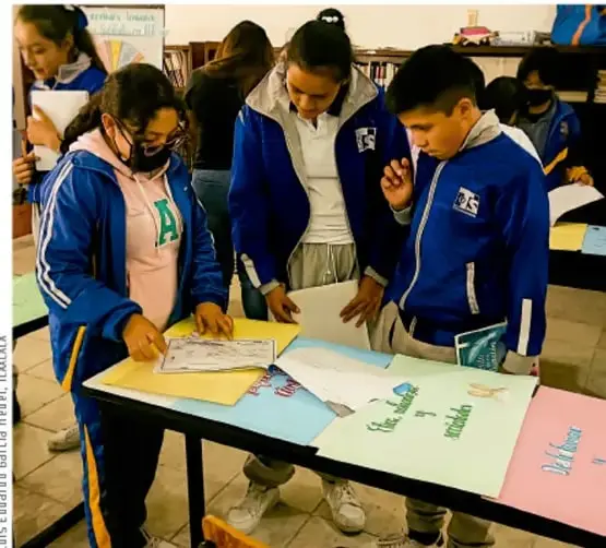 Fotografía de estudiantes de telesecundaria reunidos alrededor de una mesa, revisando cartulinas de colores con el título de un proyecto, en actitud colaborativa. Crédito: Luis Eduardo Parra M. / TLC-LAICA.