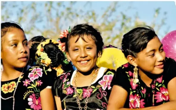 Niñas sonrientes con blusas negras bordadas con flores de colores y collares de cuentas.