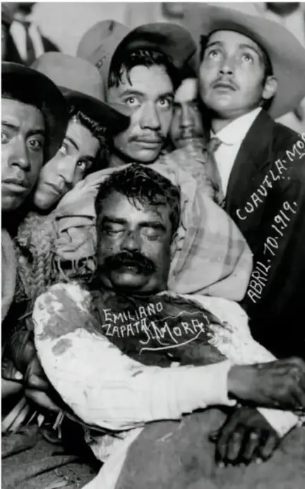 Fotografía en blanco y negro del cadáver de Emiliano Zapata rodeado por varias personas; sobre la imagen se lee 'EMILIANO ZAPATA MOR...' y 'ABRIL 10 1919'.