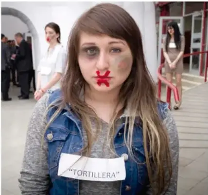 Joven con una cinta roja sobre la boca y un cartel que dice 'TORTILLERA', en una acción de protesta contra la discriminación.
