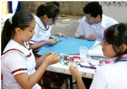 Fotografía de estudiantes trabajando en comunidad alrededor de una mesa, elaborando materiales del proyecto con papeles, colores y utensilios.