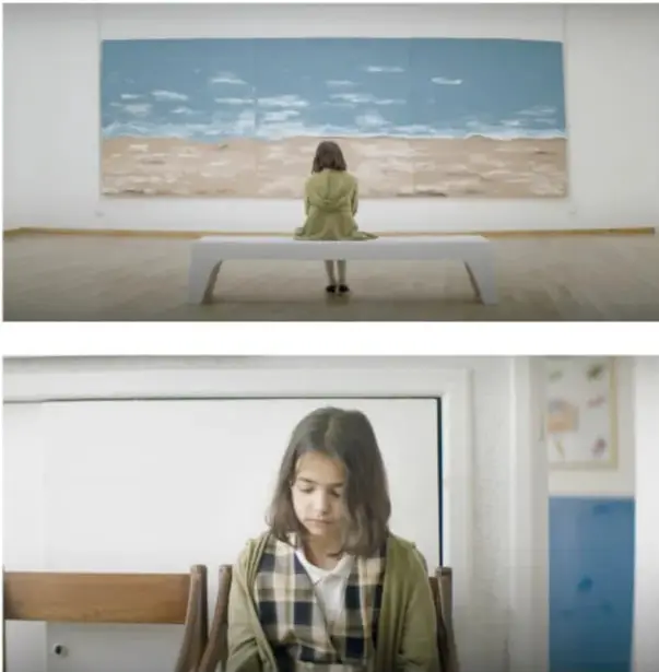 Fotograma: una niña con saco verde, de espaldas, sentada sola en una banqueta blanca frente a un gran mural de tres paneles que muestra un cielo azul con nubes y una playa desierto.