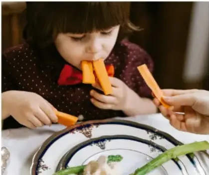 Niña comiendo zanahorias y verduras mientras sostiene los alimentos con las manos.