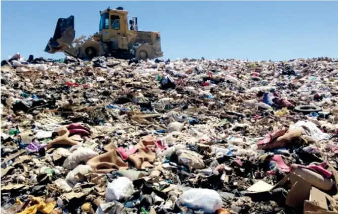 Maquinaria pesada (pala mecánica) moviendo grandes montones de basura en un tiradero a cielo abierto bajo un cielo despejado.
