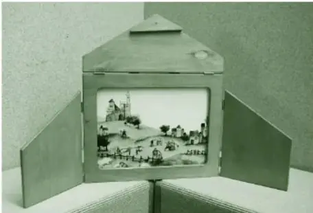 Fotografía de un teatrino kamishibai de cartón con puertas laterales abiertas como telón y una lámina ilustrada con una escena de paisaje y personajes en el centro.