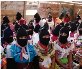 Fotografía de un grupo de personas indígenas, en su mayoría mujeres, con vestimenta tradicional y pasamontañas, reunidas en un espacio comunitario.