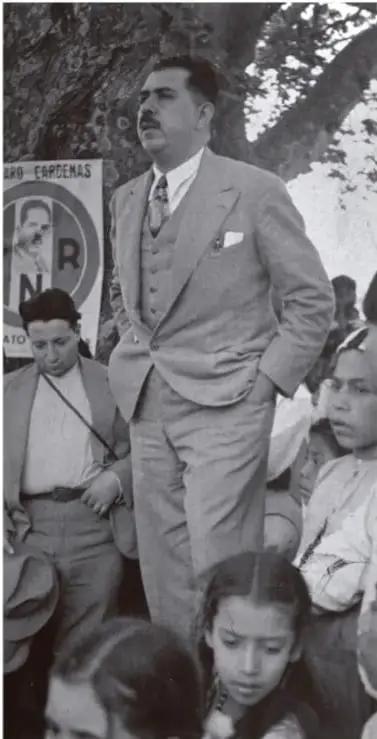 Fotografía en blanco y negro de Lázaro Cárdenas del Río acompañado de un grupo de personas, con un cartel que dice 'LÁZARO CÁRDENAS'.