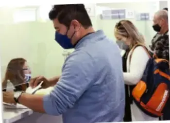 Fotografía de personas en una oficina de atención realizando un trámite, una de ellas con cubrebocas.