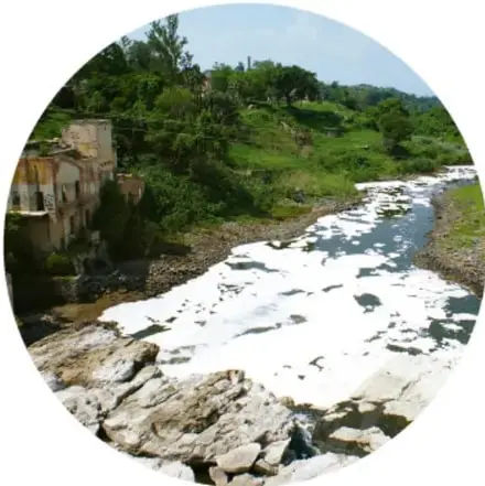 Río con espuma blanca acause de contaminación, rodeado de vegetación.