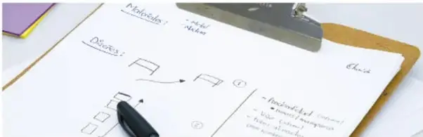 Fotografía de un cuaderno abierto sobre una mesa con bocetos de rectángulos y flechas, notas manuscritas de 'Método' y 'Diseño', un bolígrafo negro y un portapapeles con clip metálico.