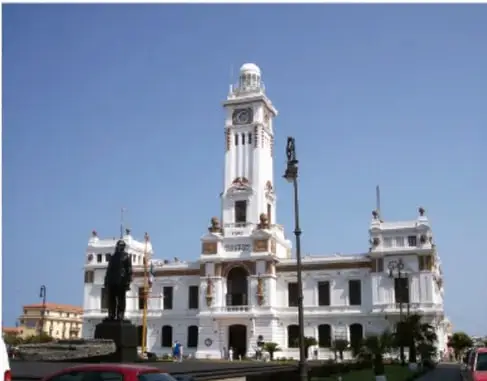 Fotografía actual a color del mismo palacio municipal, rodeado de calles, vehículos, una estatua y vegetación.