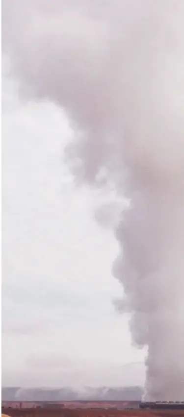 Gran columna de humo gris saliendo de una instalación industrial sobre un cielo pálido.