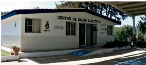 Fotografía de un edificio de un centro de salud suburbano, blanco con techo azul y señalización de estacionamiento para discapacitados.