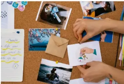 Tablero de corcho con fotos, notas y manos colocando imágenes, relacionado con la organización del evento artístico.