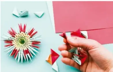 Manos doblando y cortando papel de colores para formar figuras simétricas.