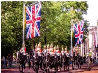 Desfile militar con banderas del Reino Unido (Union Jack) en una avenida arbolada.