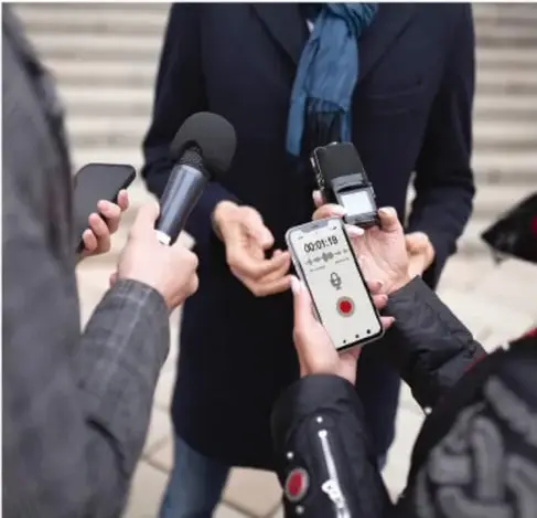 Fotografía de varias personas entrevistando a un funcionario con micrófonos y grabadoras, símbolo del papel de los medios de comunicación.