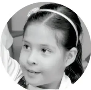 Fotografía en blanco y negro de una niña sonriente con diadema, mirando hacia un lado.