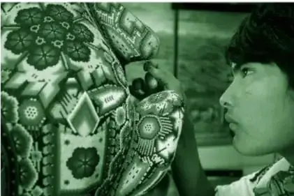 Fotografía a color (en tonos verdes en la reproducción del libro) de un joven artesano huichol de perfil, con un palillo de madera dando los últimos retoques a una gran pieza cubierta de chaquiras con figuras de flores, pájaros y formas geométricas.