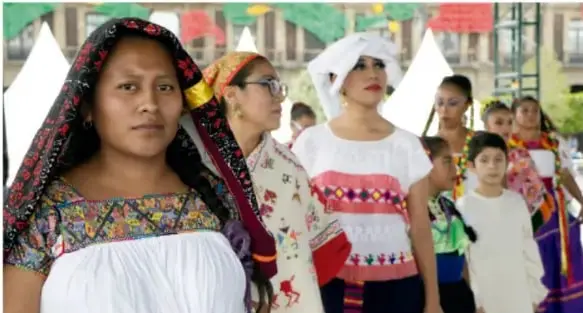 Fotografía de un grupo de niñas y mujeres con vestimenta tradicional de colores vivos, con bordados, durante un desfile o celebración comunitaria.