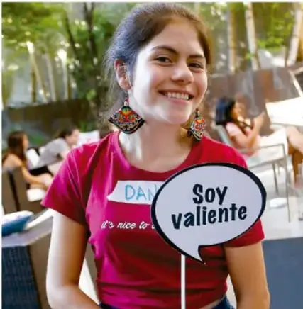 Fotografía de una joven sonriente con camiseta rosa y un cartel de palabrita que dice 'Soy valiente'.