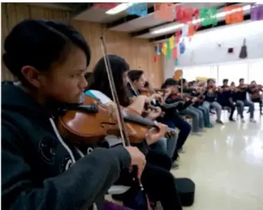 Fotografía de un grupo de niños y jóvenes tocando violines en un aula, ilustrando la práctica musical colectiva.