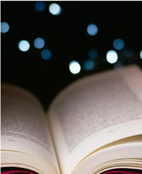 Fotografía de un libro abierto en primer plano con luces desenfocadas (bokeh) azules sobre fondo oscuro, que ilustra la lectura y la escritura del ensayo.