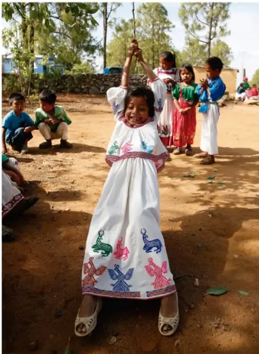 Fotografía de niñas y niños de una comunidad con vestimenta tradicional en el patio de la escuela, jugando y conviviendo al aire libre.