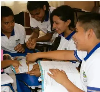 Fotografía de estudiantes de secundaria trabajando en equipo alrededor de un escritorio con cuadernos, mostrando colaboración escolar.